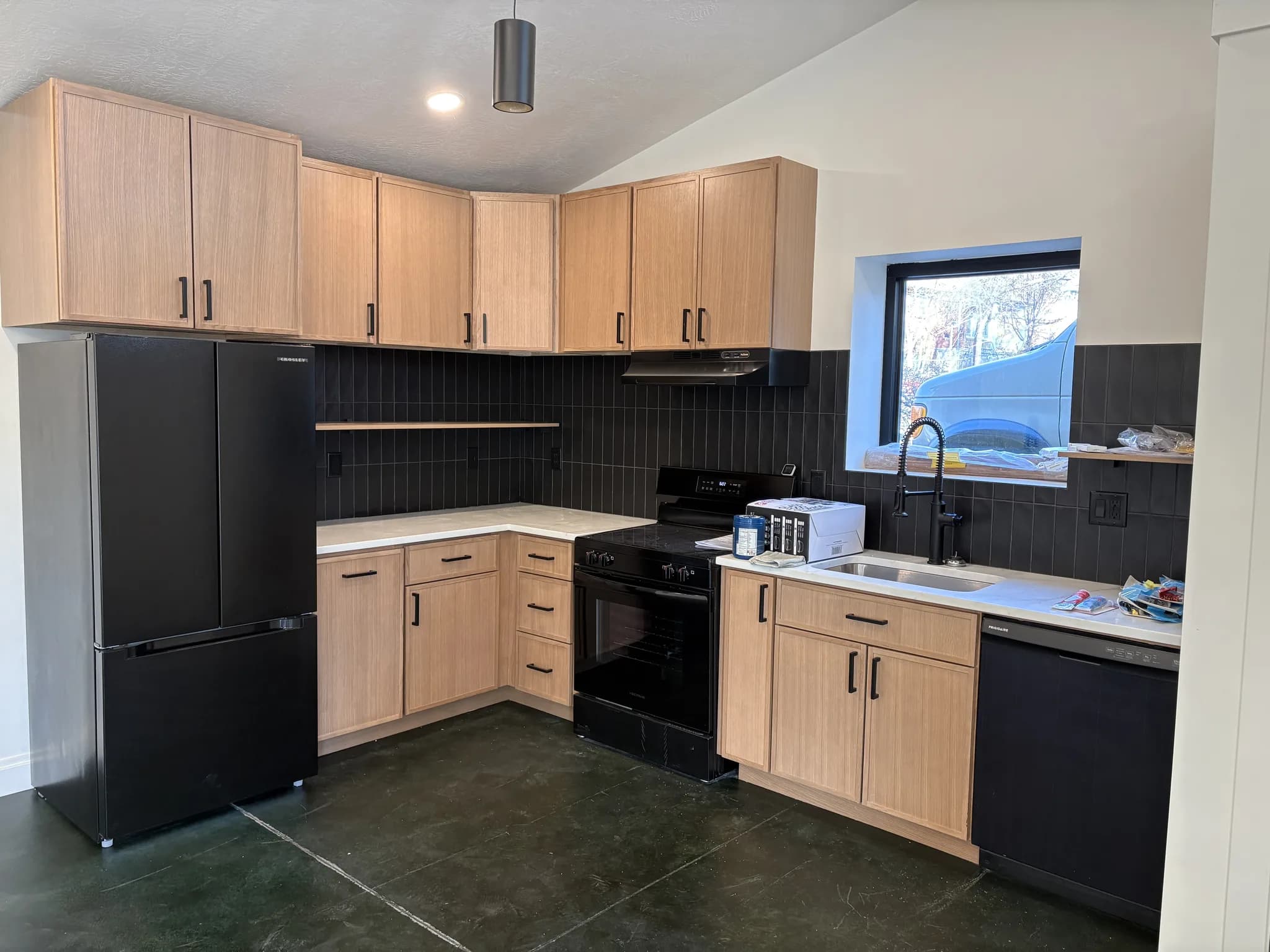 Maple kitchen with black appliances and a dark tile backsplash