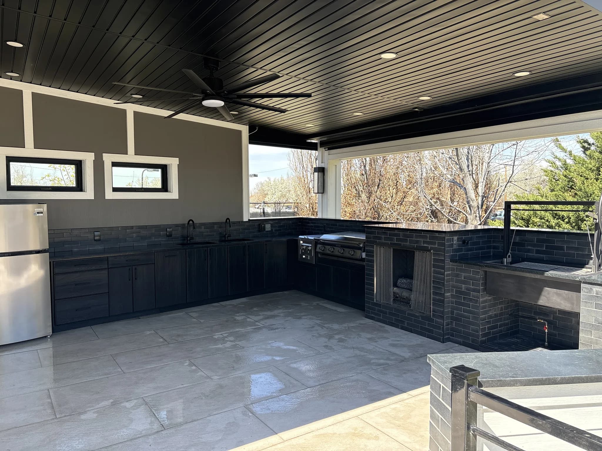 Covered outdoor kitchen with black weatherproof cabinetry and a built-in grill