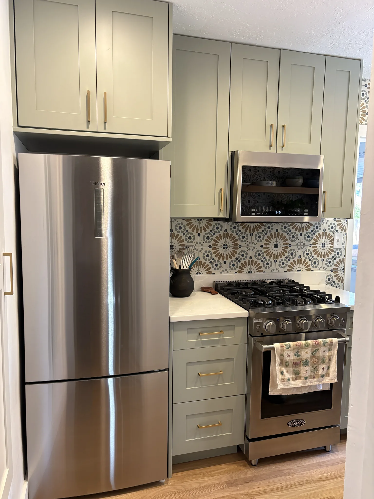 Sage green kitchen with a patterned tile backsplash and stainless range