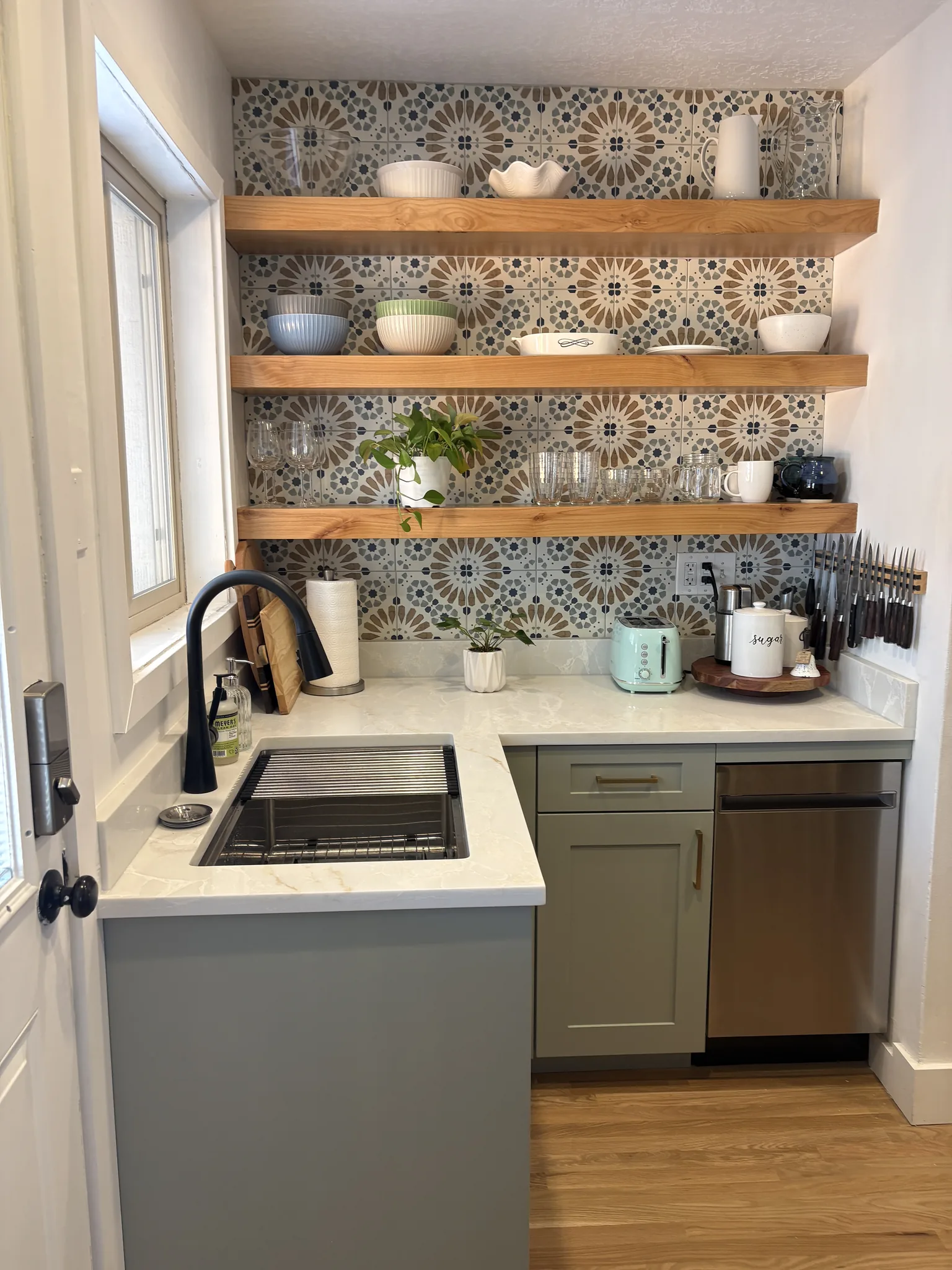Sage green kitchen with open wood shelving and a patterned tile backsplash
