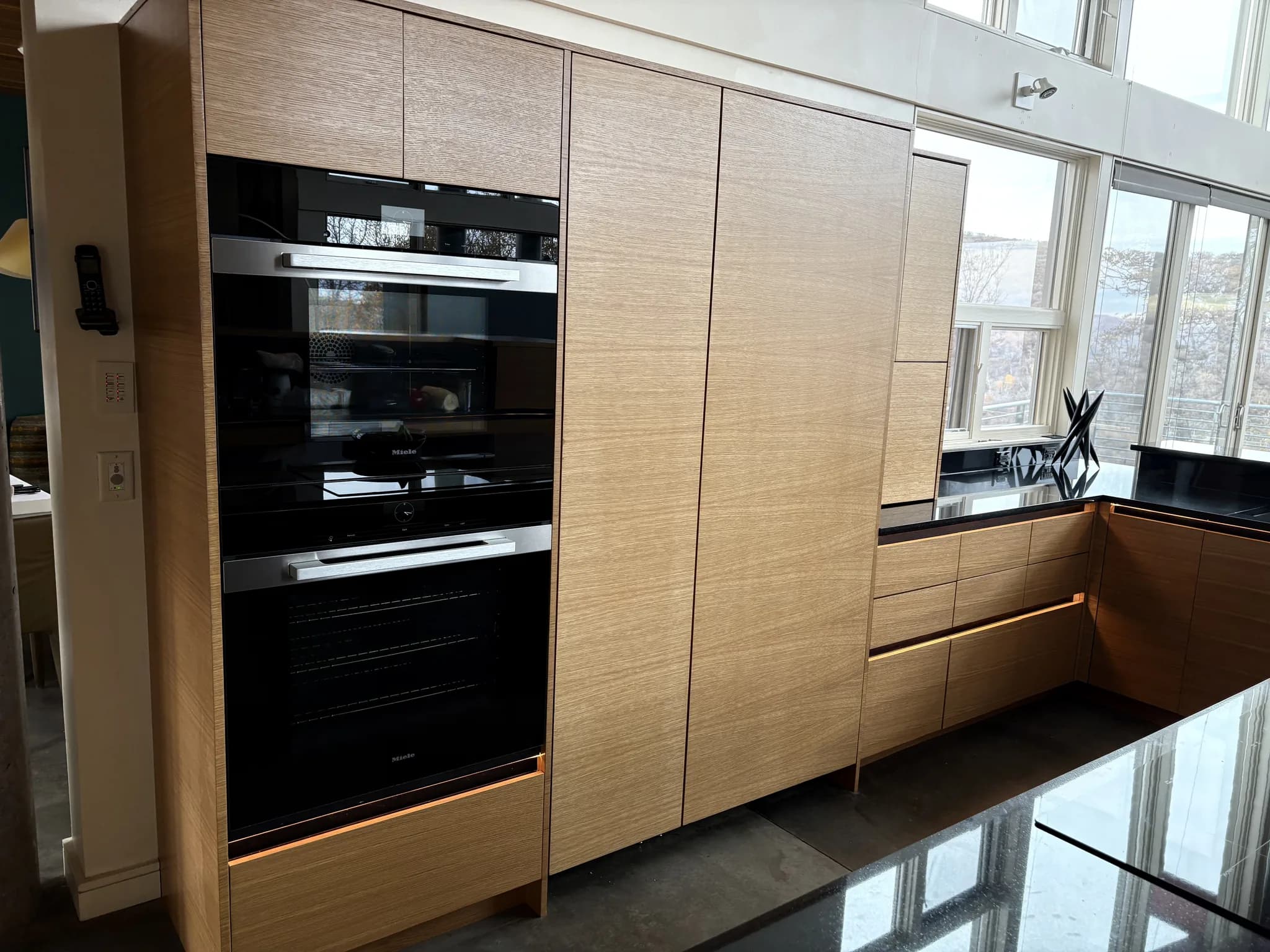 Full-height wood cabinetry wall with integrated ovens and dark countertops