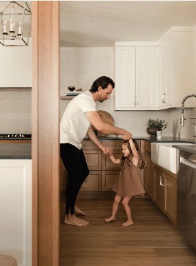 A father dancing with his daughter in a warm wood and white Shaker kitchen